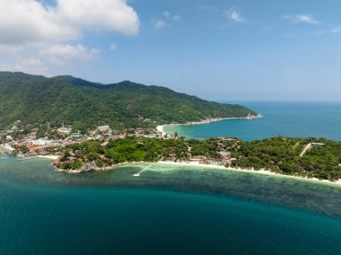 Dalgalı mavi suların ufka uzandığı kayalık bir sahile inen yemyeşil bir yamaç. Rin Nai Sahili. Haad Rin. Ko Pha Ngan, Tayland.