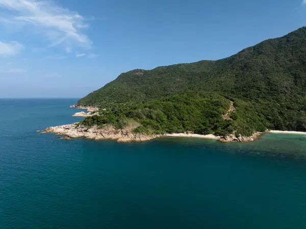 Açık mavi okyanusla buluşan yoğun yeşil tepeli kayalık kıyı şeridi. Ko Pha Ngan, Tayland.