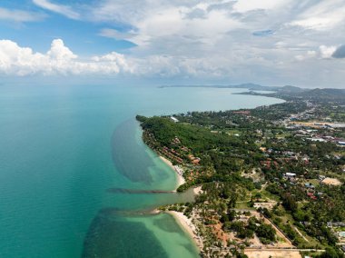 Bereketli yeşil manzaralı ve bulutlu bir gökyüzünün altında turkuaz berrak deniz manzaralı bir sahil şeridi. Koh Samui, Tayland.