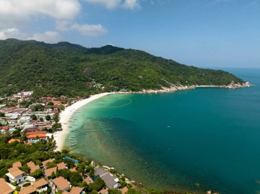 Turkuaz körfez beyaz kumlu bir plajla kaplı ve güneşli bir gökyüzünün altında yemyeşil tepelerle çevrili. Haad Rin. Ko Pha Ngan, Tayland.
