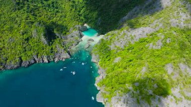 Turkuaz üzerinde turist botları olan gizli bir koy ve göl, kayaların oluşumlarını kaplayan suları ve yemyeşil alanları besler. El Nido. Palawan, Filipinler.