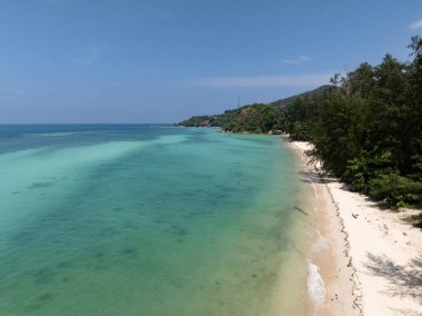 Turkuaz suları, beyaz kumları ve açık mavi gökyüzünün altında dağınık yeşillikleri olan tropik kıyı şeridi. Ko Pha Ngan, Tayland.