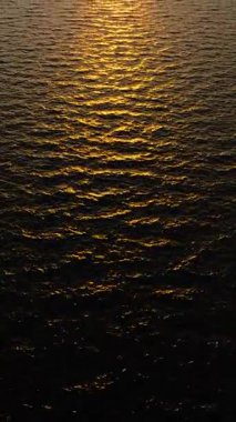 Gün batımının ılık turuncu parıltısı canlı bir gökyüzünün altındaki dalgalı okyanus dalgalarını yansıtıyor. Koh Tao, Tayland.