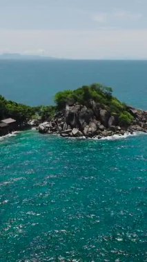Yoğun yeşil bitki örtüsü olan küçük bir ada güneşli bir gökyüzünün altında turkuaz sularla çevrili. Koh Tao, Tayland.