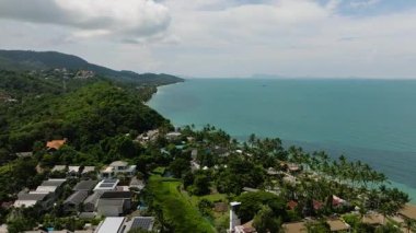Yoğun yeşillik, dağınık evler ve bulutlu bir gökyüzünün altında turkuaz okyanus manzarası. Ko Samui, Tayland.