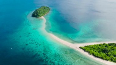El değmemiş bir kum yığını, turkuaz ve gök mavisi sularla çevrili iki yemyeşil adayı birbirine bağlar. Bon Bon Plajı, Romblon, Filipinler.