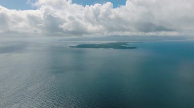 Bulutlu bir gökyüzünün altında dalgalanan okyanus sularıyla çevrili sakin bir ada. San Jose, Romblon. Filipinler.