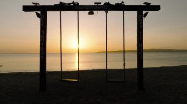 Güneşin sakin bir okyanusun üzerinde battığı kumlu bir sahilde salıncak silueti. Santa Fe, Tablo, Romblon, Filipinler.
