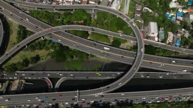Yoğun kentsel alanlardan geçen yoğun bir otoyol döngüsünün üst görüntüsü arabalar ve çevreleyen yeşillikler. Bangkok, Tayland.