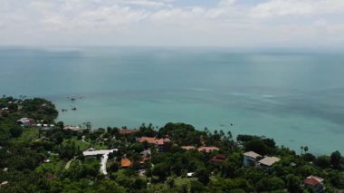 Parlak bir gökyüzünün altında ufka uzanan sakin bir okyanusla çevrili bir sahil köyü. Ko Samui, Tayland.