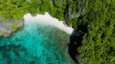 Serenity Sahili 'nin etrafındaki kireçtaşı kayaları beyaz kum, turkuaz deniz suyu ve mercanlarla kaplı. El Nido. Palawan, Filipinler.