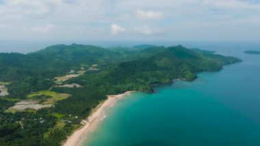 Kristal berrak turkuaz sular kıyı manzarasıyla harmanlanır. Kıyı şeridi, beyaz kumlar üzerinde güzel dalgalar. Dagmay Sahili. El Nido, Palawan. Filipinler.