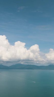 Turkuaz deniz, canlı bulutlu bir gökyüzünün altındaki uzak dağlara uzanır ve huzurlu bir manzara yaratır. Ko Pha Ngan, Tayland.