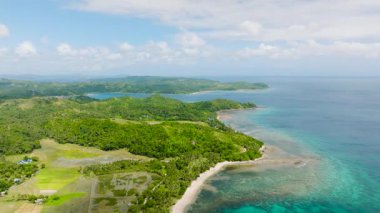 Turkuaz suların ve açık mavi gökyüzünün altında yemyeşil tepelerin bulunduğu çarpıcı bir sahil şeridi. Santa Fe, Tablo, Romblon, Filipinler.