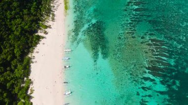 Turkuaz su ve kıyı şeridi boyunca yoğun yeşil orman bulunan beyaz kumlu bir plajın havadan çekilmiş görüntüsü. Puka Kabuğu, Boracay Adası, Filipinler.