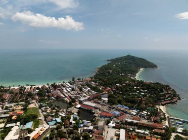Tepeler ve yeşilliklerle çevrili, turkuaz sularla çevrili temiz mavi gökyüzünün altında kumlu kıyılarla karşılaşan bir kasaba. Ko Pha Ngan, Tayland.