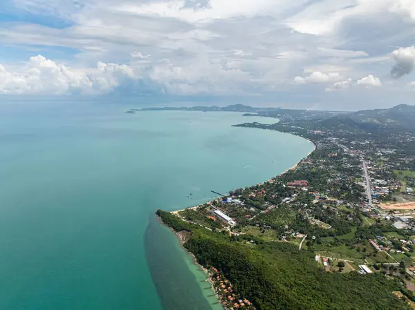 Parçalı bulutlu bir gökyüzünün altında yemyeşil ve mavi deniz olan tropikal kıyı şeridinin insansız hava aracı görüntüsü. Koh Samui, Tayland.
