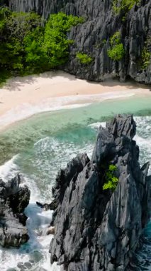 Matinloc Adası 'ndaki beyaz kumsala dalgalar çarpıyor. El Nido, Palawan. Filipinler. Dikey görünüm.