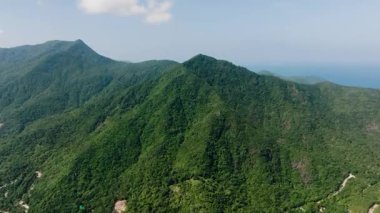 Parlak mavi gökyüzünün altında yoğun tropikal ormanlarla kaplı yemyeşil dağ zirveleri. Ko Pha Ngan, Tayland.
