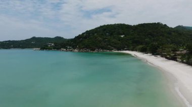 Beyaz kumlu sahil ve turkuaz su. Arkasında orman tepeleri var. Tanga Nai Pan Yai Sahili. Ko Pha Ngan, Tayland.