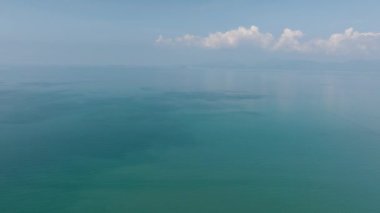 Uçsuz bucaksız mavi gökyüzü ve uzak dağların altında bulutların soluk yansımalarıyla sakin bir turkuaz deniz. Ko Samui, Tayland.