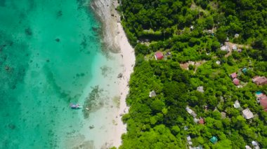 Beyaz kumlu, yemyeşil yemyeşil ve turkuaz renkli parlak gökyüzü altında manzaralı tropikal bir sahil. Hagdan Sahili, Boracay Adası, Filipinler.