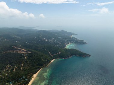 Parlak mavi gökyüzünün altında turkuaz suları ve beyaz kumlu plajları olan yemyeşil bir sahil manzarası. Ko Pha Ngan, Tayland.
