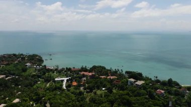 Berrak bir gökyüzü altında yemyeşil bitki örtüsü ve sakin turkuaz sularla çevrili deniz kenarı köyü. Ko Samui, Tayland.