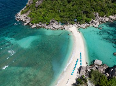 Turkuaz suyla kaplı, mavi şemsiyelerle kaplı ve yemyeşil bir kumsalda. Nangyuan Adası Sahili, Tayland.