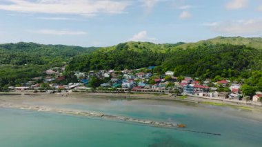 Hareketli bir sahil kasabası yuvarlanan yeşil tepelerin arasına yerleşmiş ve berrak okyanus sularıyla çevrelenmiş. Santa Fe, Tablo, Romblon, Filipinler.