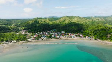 Yeşil tepelerle çevrili kıyı köyü ve parlak bir gökyüzünün altında turkuaz su. Santa Fe, Tablo, Romblon, Filipinler.
