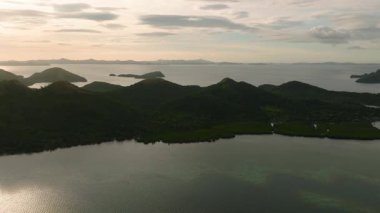 Esmer bulutların altında yeşil tepeler ve mangrov ormanları olan el değmemiş bir ada. Coron, Palawan, Filipinler.