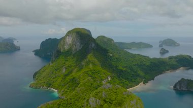 Bereketli yeşil dağların sakin mavi okyanusla buluşması dramatik bir manzara. Plajları ve kireçtaşı kayalıkları olan tropik adalar. Cadlao Adası. El Nido, Palawan. Filipinler.