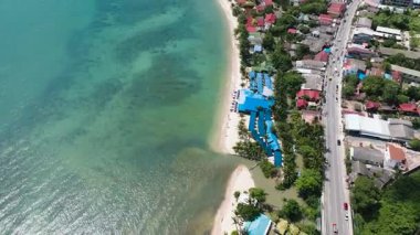 Kumsalın yanındaki sahil yolu ve turkuaz deniz, tropikal evler ve parlak güneş ışığı altında yeşillik. Ko Samui, Tayland.