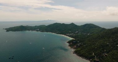 Parçalı bulutlu bir gökyüzünün altında sakin mavi suları olan yeşil tepeler ve kıyı şeridi. Ko Tao, Tayland.