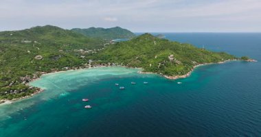 Sivri kayalar ve yeşil tepeler mavi gökyüzünün altında kristal berrak turkuaz suları çevrelemektedir. Koh Tao, Tayland.