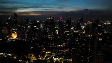 Gökdelenler gökyüzünü aydınlatıyor, yüksek binalar gece gökyüzüne karşı aydınlanıyor. Bangkok, Tayland.