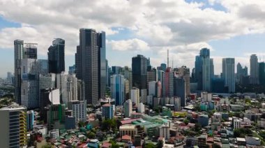 Modern gökdelenler parlak bir gökyüzünün altında yerleşim binalarıyla çevrili. Metro Manila, Filipinler.