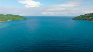 Bereketli yeşil kıyılarla çevrili dar bir su yolu açık okyanusa, parlak mavi bir gökyüzünün altına açılıyor. Romblon, Filipinler.