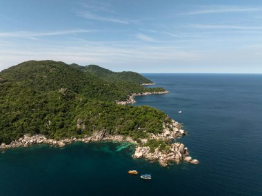 Yakınlarda birkaç küçük tekne bulunan yemyeşil burunlar turkuaz suları sakinleştirmek için uzanıyor. Tayland, Koh Tao.
