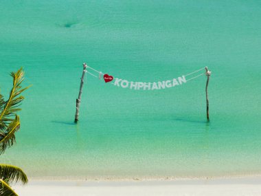 Koh Phangan tabelası güneşli bir gökyüzünün altında beyaz kumlu bir sahile yakın turkuaz suların üzerinde sergileniyordu. Ko Pha Ngan, Tayland.