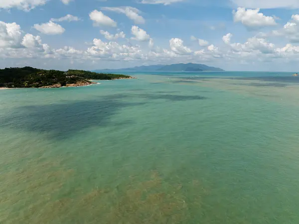 Turkuaz suları, gölgeli bölgeleri ve açık gökyüzünün altında beyaz bulutlu uzak dağları olan kıyı bölgesi. Koh Samui, Tayland.