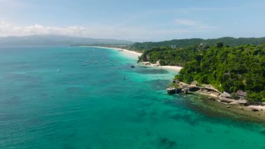 Canlı turkuaz suyla kıyı şeridi, yemyeşil çevre ve dağınık geleneksel tekneler. Boracay Adası, Filipinler.