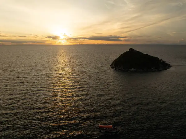 Altın gün batımı, uzak bir ada ve küçük bir tekne ile denizi yansıtır. Tayland, Koh Tao.