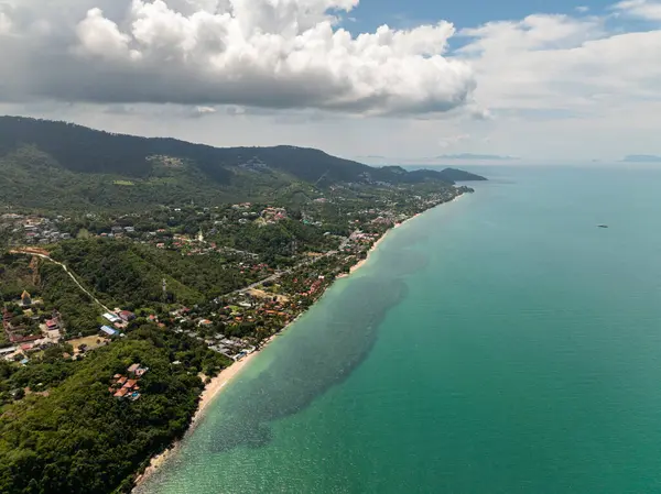 Yeşil tepeleri ve ufuk çizgisine uzanan berrak sularıyla dramatik bulutlu bir gökyüzü altında tropik kıyı şeridi. Koh Samui, Tayland.