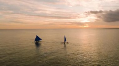 Mavi yelkenli yelkenliler, sakin sulara yansıyan sakin bir günbatımında altın rengi ile. Boracay Adası, Filipinler.