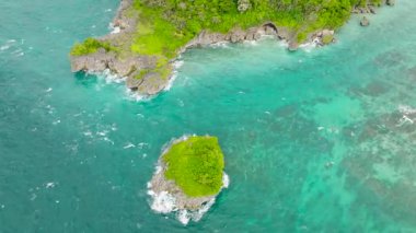 Kayalık kenarları ve beyaz dalgaları olan turkuaz okyanus sularıyla çevrili küçük canlı yeşil bir ada. Boracay Adası, Filipinler.