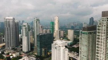 Modern bir şehirde kentsel yeşillik parçalarıyla ufuk çizgisine egemen olan uzun binalar. Metro Manila, Filipinler.