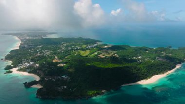 Turkuaz sular yemyeşil tepeler ve dağınık bulutların altında kumlu plajlarla buluşuyor. Boracay Adası, Filipinler.