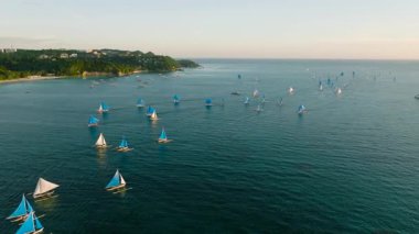 Berrak tropikal kıyı şeridi, yemyeşil bir sahil şeridinde mavi yelkenli tekneler geziniyor. Boracay Adası, Filipinler.